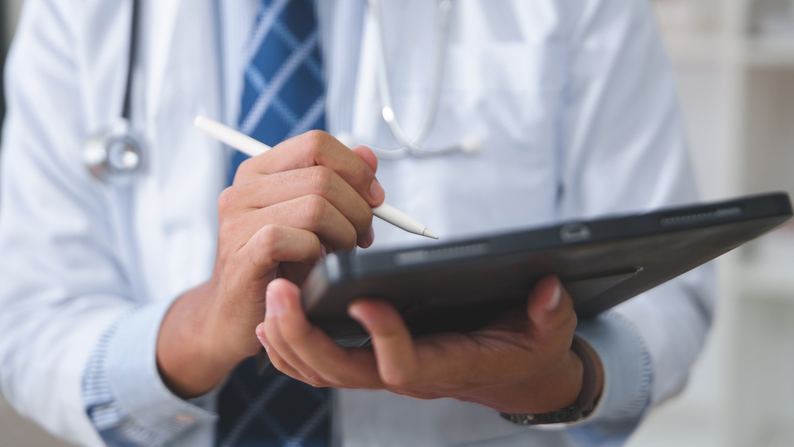 Médico con bata blanca y estetoscopio revisando ficha clínica en una tablet